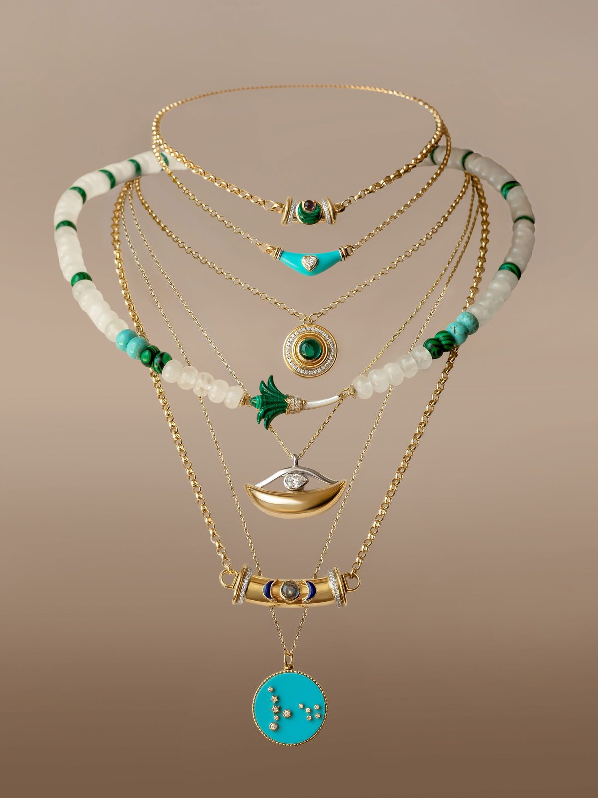 Seven necklaces layered together — a beaded moonstone and malachite strand, a turquoise heart bar, a malachite cabochon medallion and a diamond eye pendant.