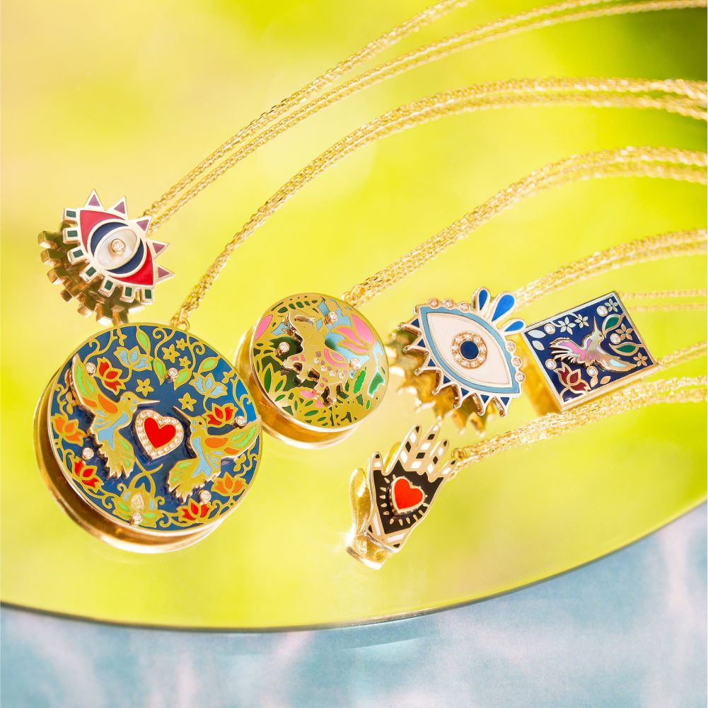 Rich Kitsch pieces on a lime mirror — a hand-painted locket of birds and flowers, an eye ring, a sunburst eye charm and a hand ring holding a red heart.