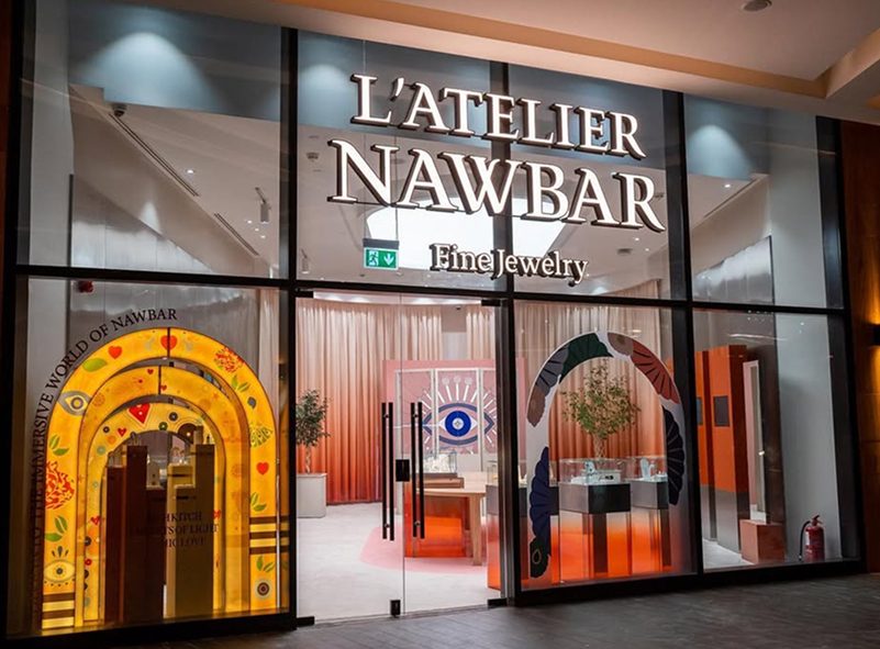 The L'Atelier Nawbar Fine Jewelry boutique at night, its windows painted with golden arches, an eye motif and blossoming vines.
