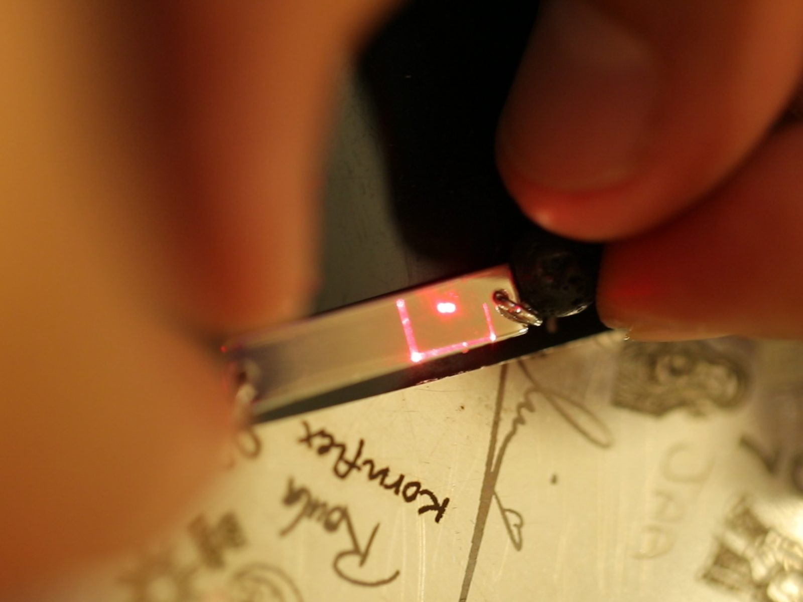 A name being laser-engraved inside a gold band, the artisan steadying the ring beneath the red guide light.