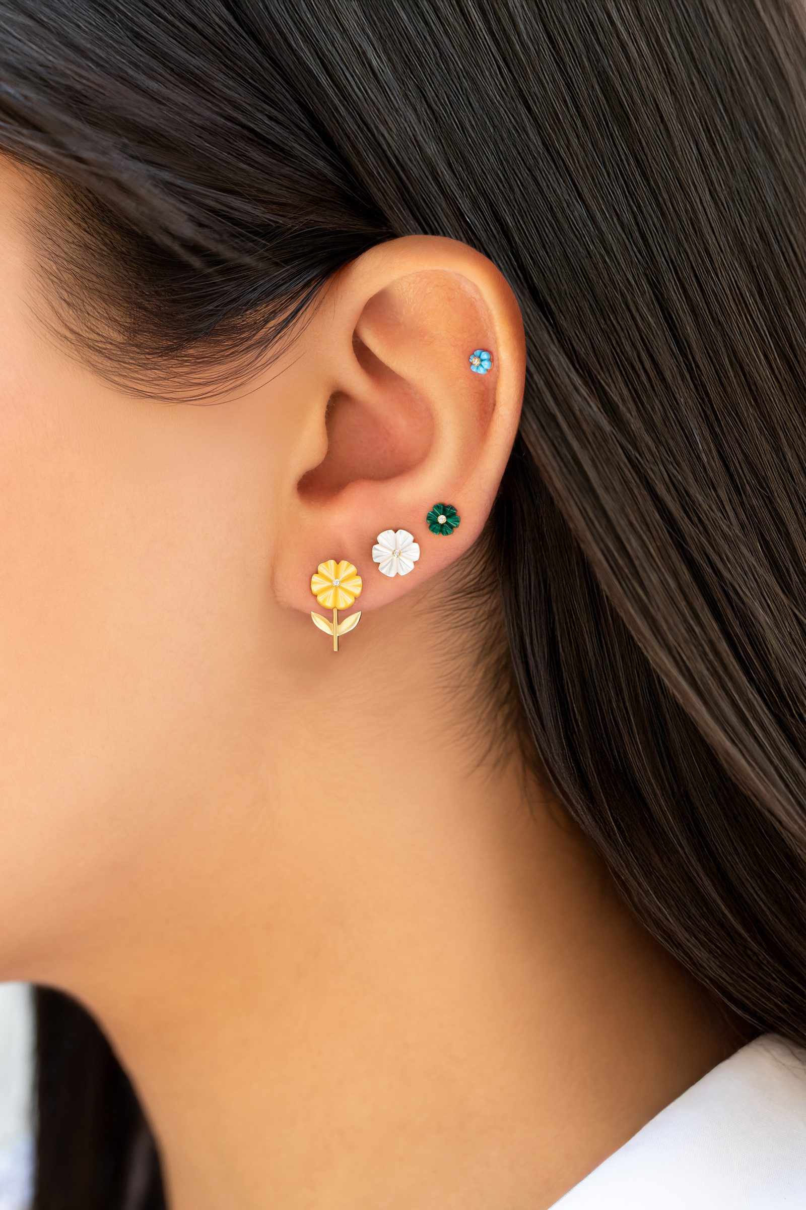 A curated ear stack: carved flower studs in yellow, white and green, with a turquoise blossom high on the helix.