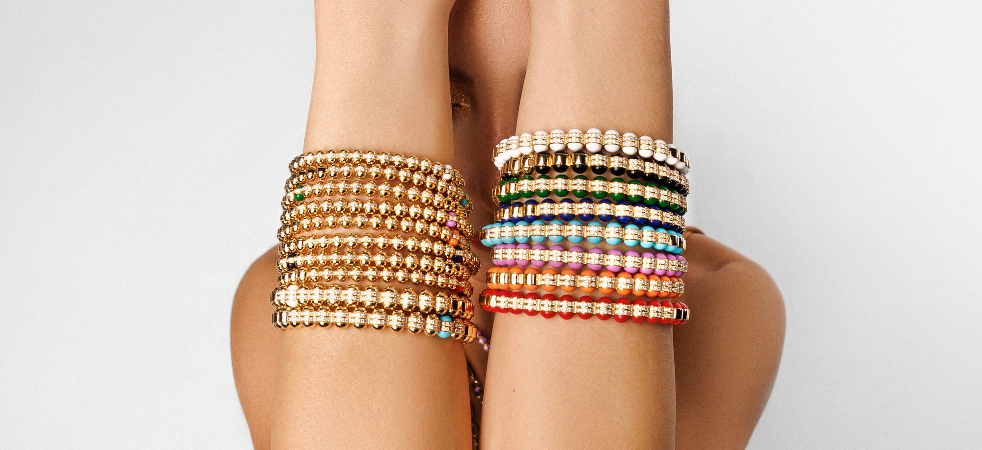 Two wrists stacked with Atoms bracelets — beaded gold set with diamonds and rows of turquoise, lapis, coral and black enamel.